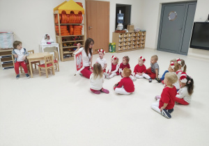 Dzieci siedzą na podłodze i oglądają pokazywane przez panią godło Polski.
